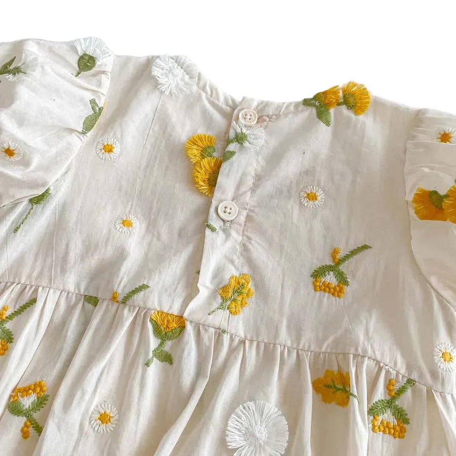 Close up of the upper back on a white cotton baby romper showing two white button closures and yellow floral embroidery.