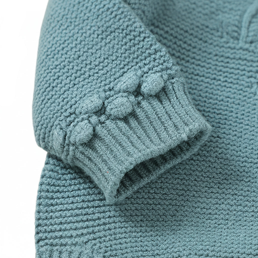 Close-up of the textured bobble-knit accent trim on the long sleeve cuff of the teal seamless sweater romper.