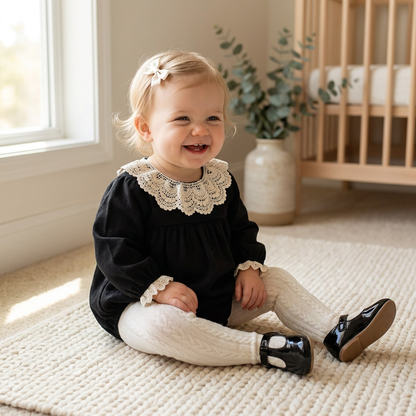 Infant girl wearing black vintage lace collar long sleeve bubble romper sitting in a nursery