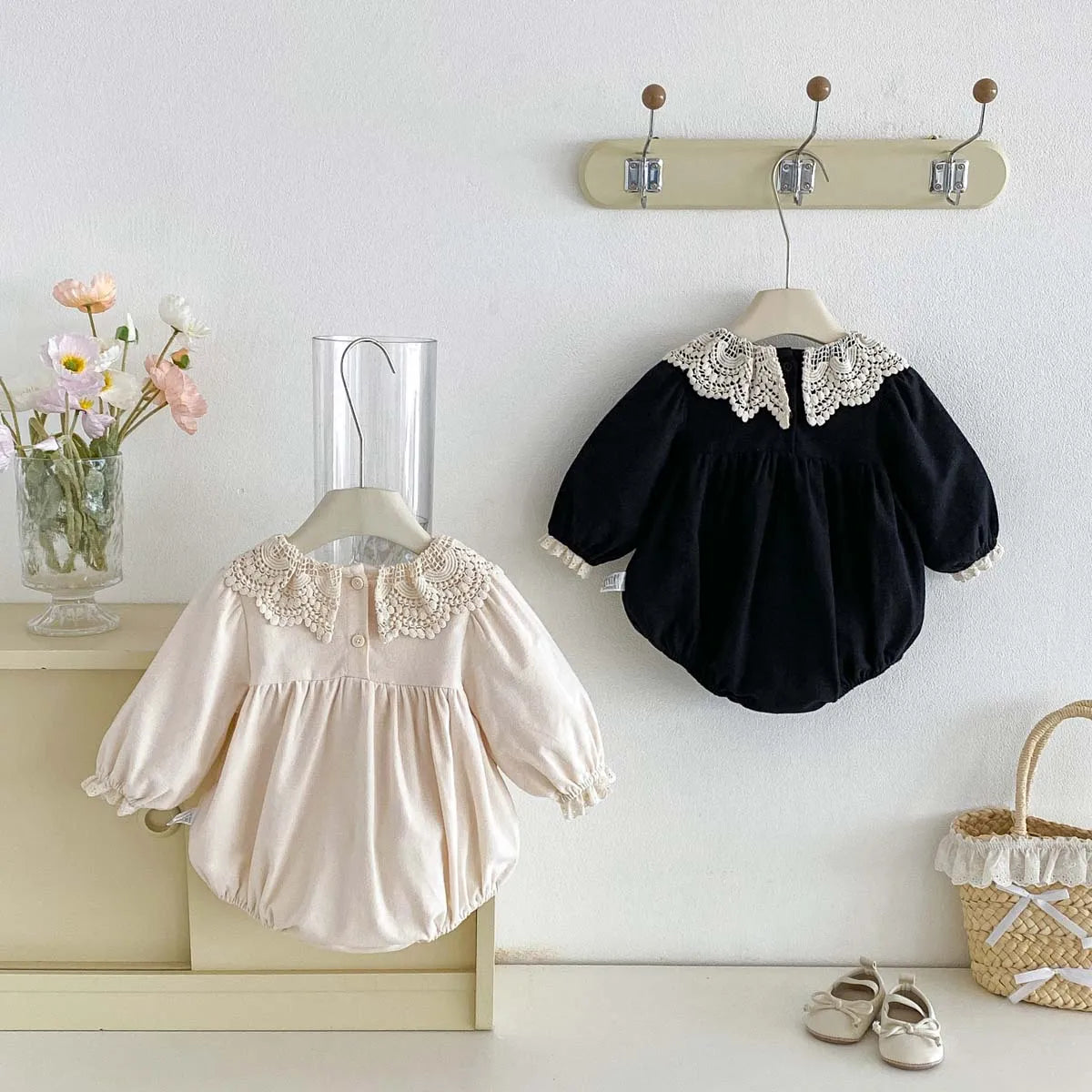 Cream and black long sleeve baby girl lace collar rompers hanging on a wooden wall rack