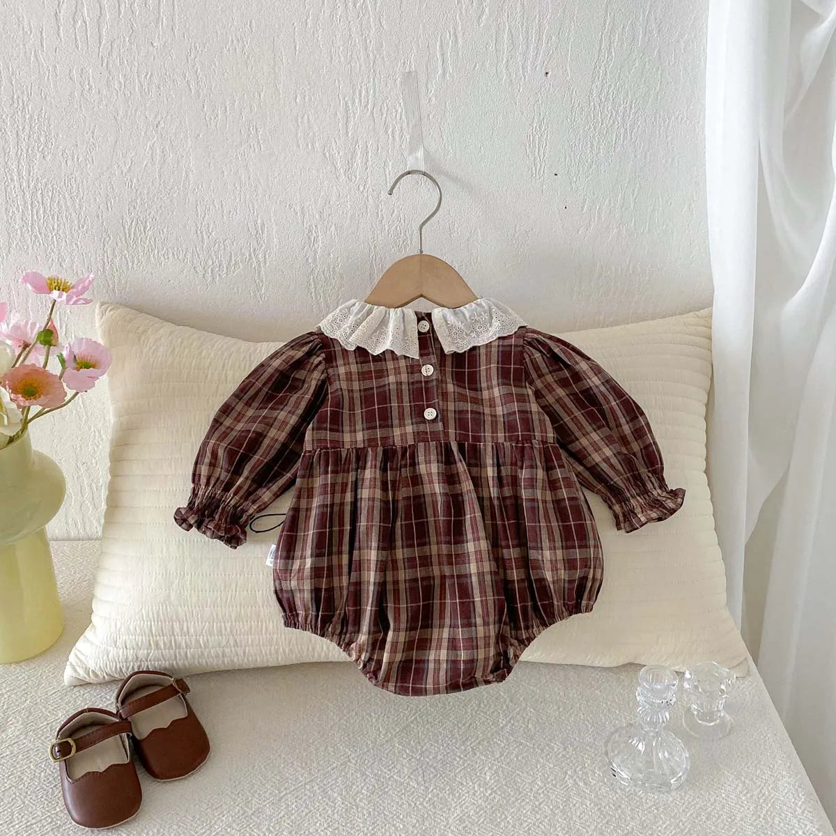 Brown plaid baby girl long sleeve bubble romper hanging on a wooden hanger with matching shoes nearby.
