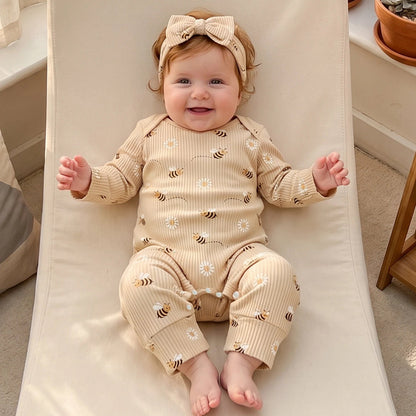 Smiling baby girl wearing the Kidsely ribbed bee and daisy print romper and headband set while lying comfortably on a white chair.