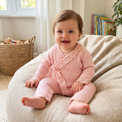 Happy baby girl sitting on a soft beige cushion wearing the pink pointelle knit kimono romper.