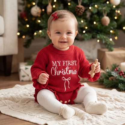 Baby girl sitting in front of a Christmas tree wearing a red My First Christmas knit sweater romper and white tights.