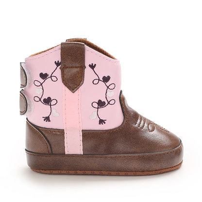 Side view of a pink and brown baby cowboy boot highlighting the embroidered vine and heart details.