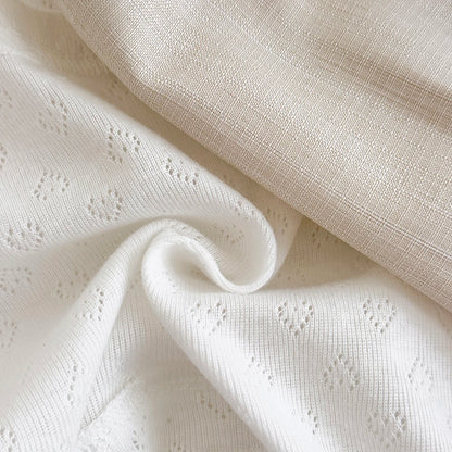 Detailed view of the breathable white eyelet pointelle knit fabric with a subtle heart pattern used for the infant bodysuit.