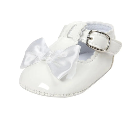 Side angle view of a single baby girl white patent leather T-strap Mary Jane dress shoe featuring a clean white satin ribbon bow.