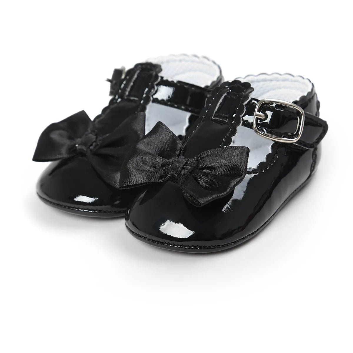 Black patent leather T-strap Mary Jane dress shoes for baby girls featuring a satin bowknot and an adjustable buckle strap on a clean white background.