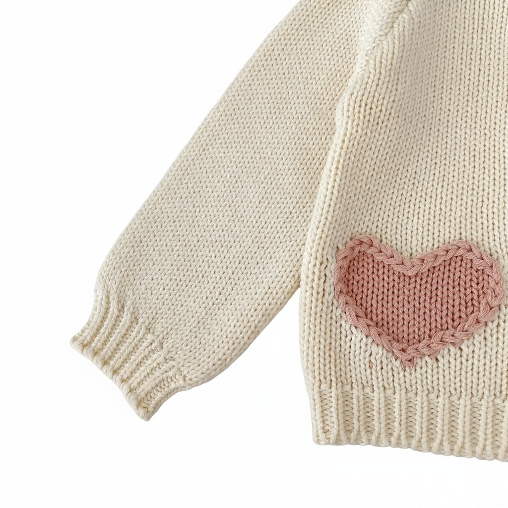 Side view of long sleeve and pink heart accent pocket on cream baby knit sweater.