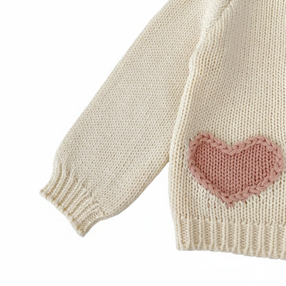 Side view of long sleeve and pink heart accent pocket on cream baby knit sweater.