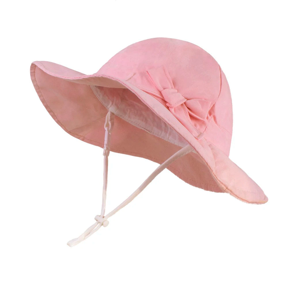 A light pink 100% cotton wide brim sun hat for baby and toddler girls featuring an adjustable chin strap and a decorative side bow.