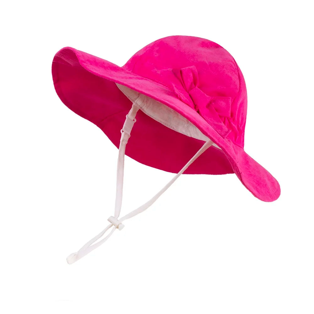 Vibrant rose pink 100% cotton wide brim sun hat for baby and toddler girls featuring an adjustable strap and side bow detail.