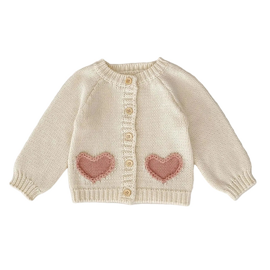 Cream knitted cardigan sweater for baby girls with pink heart pockets and front buttons.