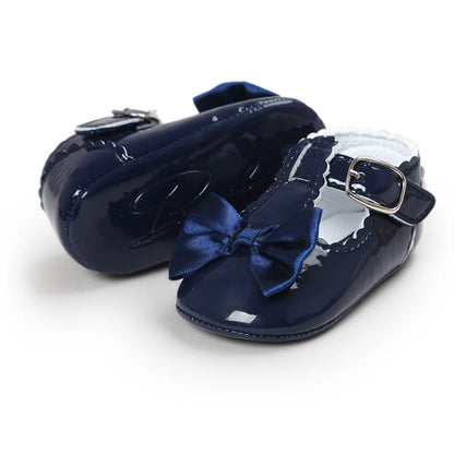 Deep navy blue patent leather baby girl T-strap Mary Jane dress shoes featuring a dark blue satin bowknot overlay.