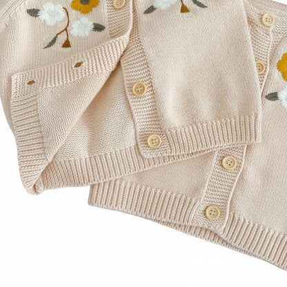 Close-up texture of soft oatmeal knit fabric and button detail on baby cardigan sweater.