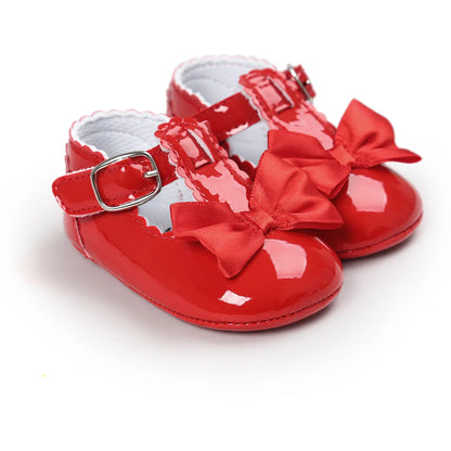 Vibrant red patent leather baby girl T-strap dress shoes featuring a matching red satin bow and buckle strap on a clean white background.