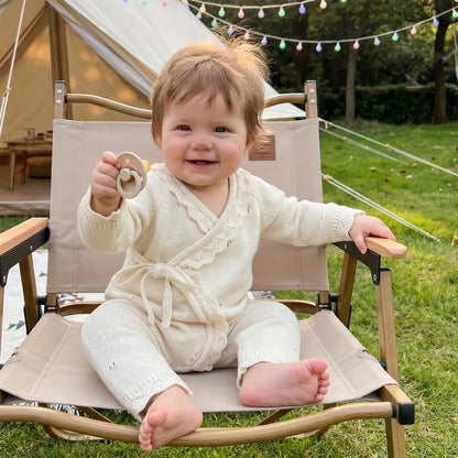 Baby girl sitting in a small outdoor folding chair wearing the ivory pointelle knit kimono romper.