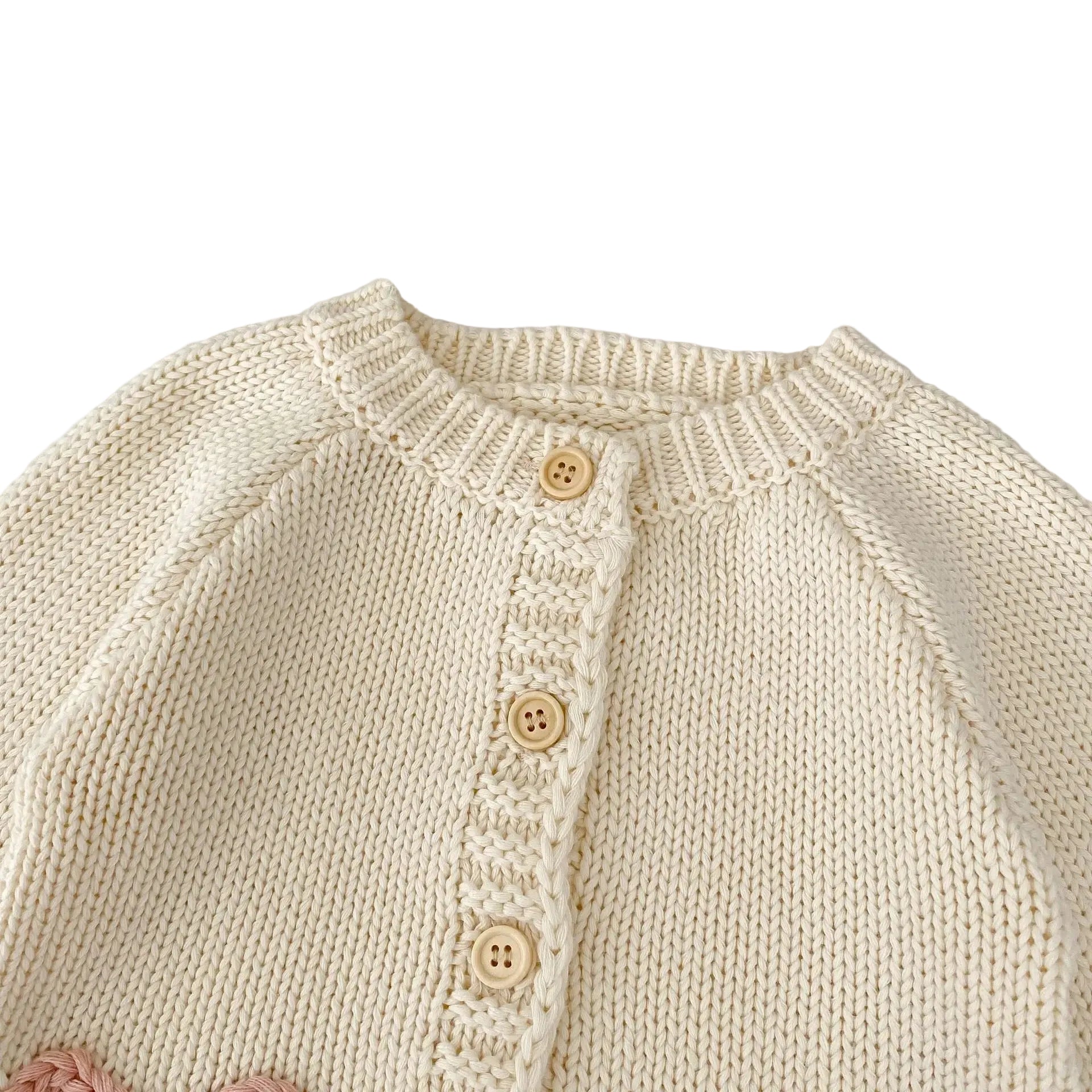 Close-up of ribbed crew neckline and top buttons on cream baby girls cardigan.