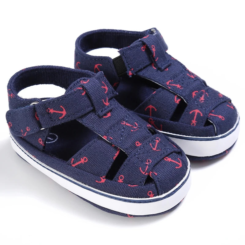 A pair of navy blue baby canvas sandals with a red nautical anchor print.