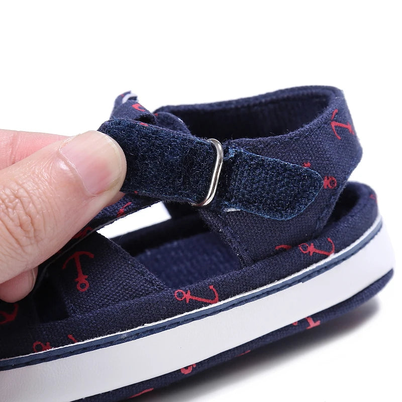Close-up of a hand opening the adjustable velcro strap on a navy blue nautical baby sandal.