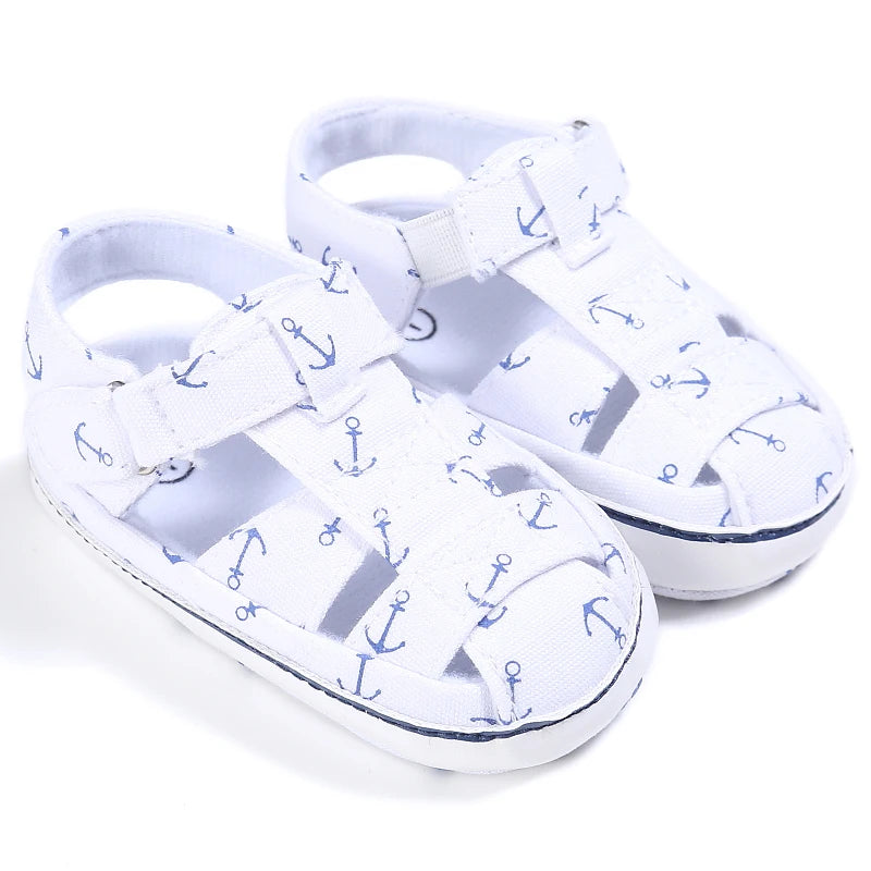 A pair of crisp white baby canvas sandals with a blue nautical anchor print.