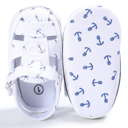 Top down and bottom sole view of a white baby canvas boat shoe showing the blue anchor anti-slip grip pattern.