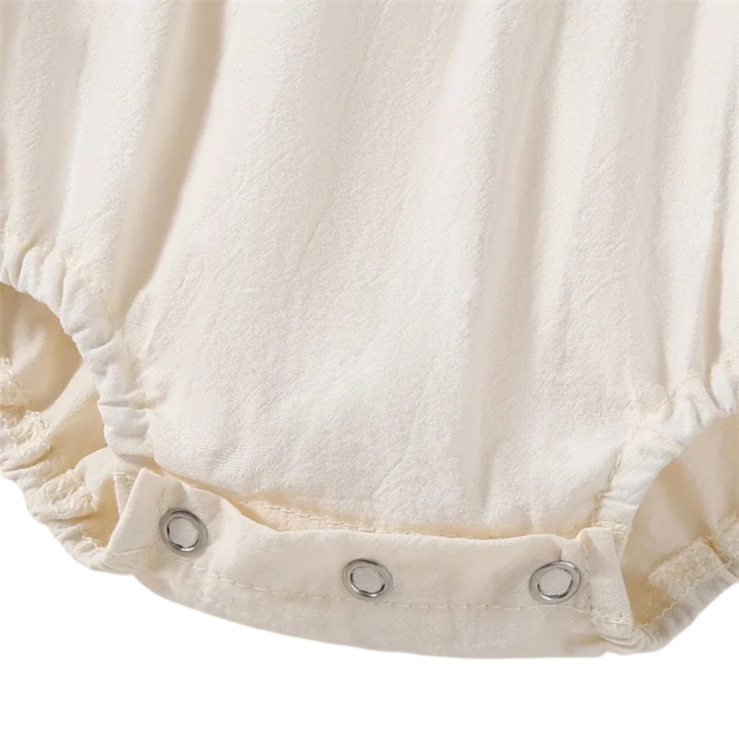 Close-up of the bottom diaper area of the cream baby romper highlighting the secure three-metal snap button closure system.