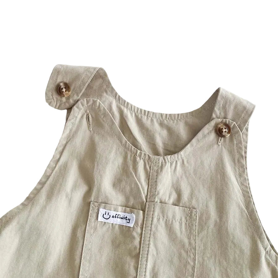 Close up of the Hamptons Beige baby overalls highlighting the adjustable button shoulder straps and front chest pocket.