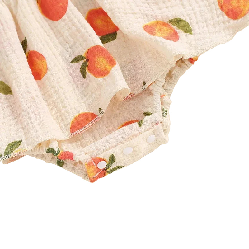 Close-up showing the bottom snap closures for easy diaper changes on the baby girl peach print romper dress.
