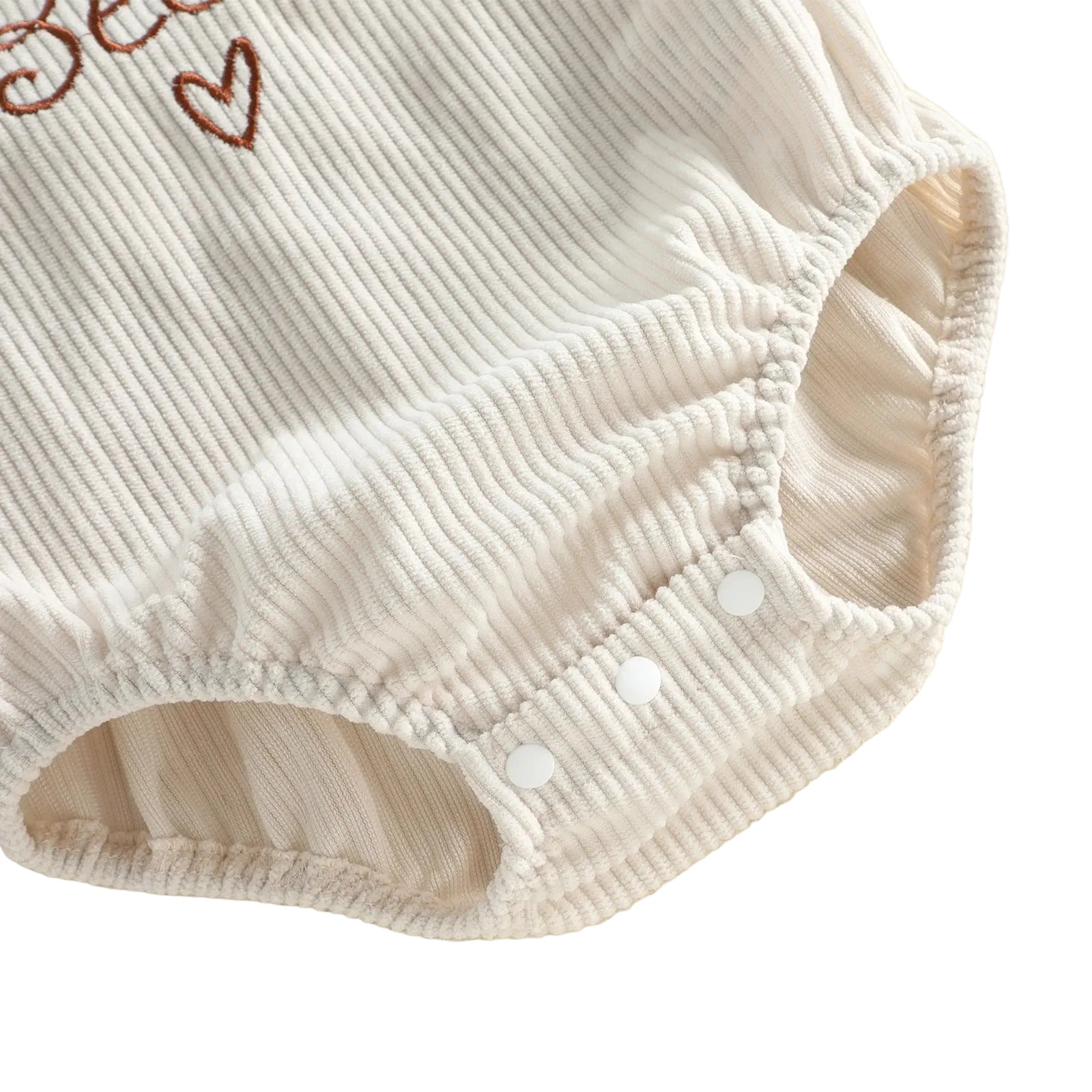 Close-up of the bottom gusset on the beige corduroy baby romper, showing the three white snap closures designed for easy diaper changes.