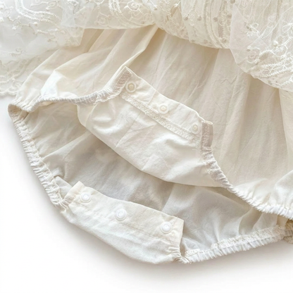 Close-up showing the soft cotton lining and bottom snap closures of a baby girl lace romper.