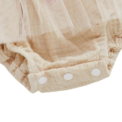 Close up view of snap button closures on cream baby girl romper jumpsuit for easy diaper changes