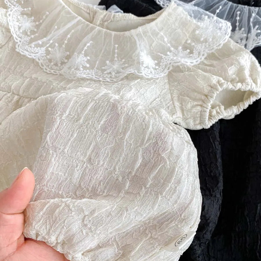 Close-up detail of the intricate floral embroidery and breathable popcorn seersucker texture on a boutique baby romper.