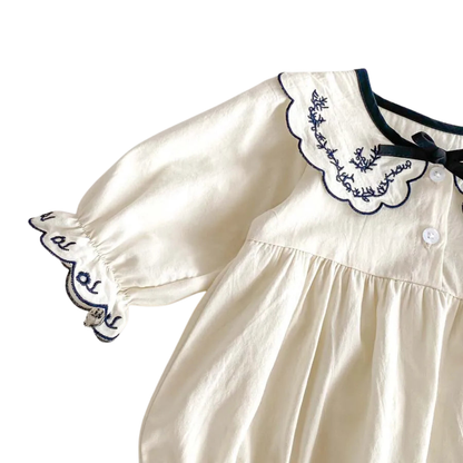 Detail view of the front button-up placket on the ivory cotton romper under the embroidered scalloped collar.