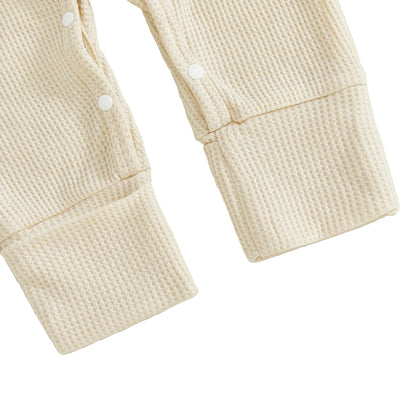 Close-up of the ribbed cuffs and secure snap closures on the legs of the beige waffle knit baby romper.