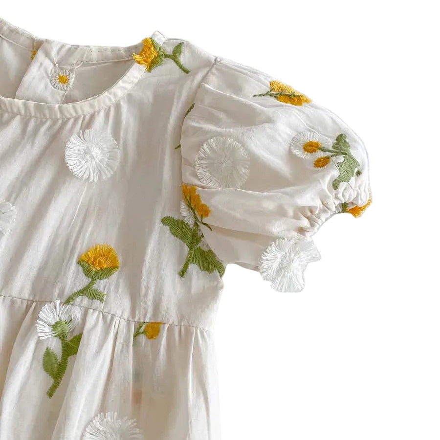 Close up of the round neckline and short puff sleeve on a white baby girl romper featuring yellow tufted floral embroidery.