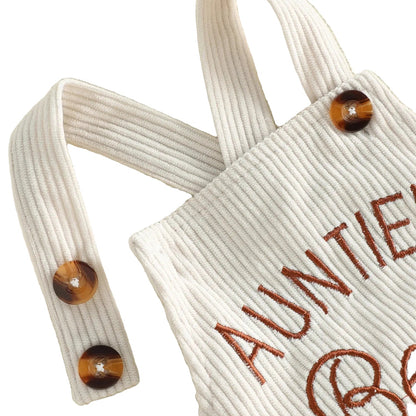 Close-up detail of the beige ribbed corduroy fabric and dual faux tortoiseshell buttons on the shoulder suspender strap of the baby romper.