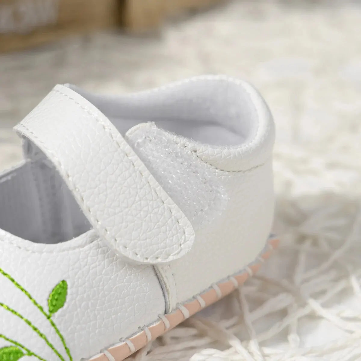 Close-up on the heel and adjustable strap of a white baby girl shoe, highlighting the soft interior padding and stitching detail.
