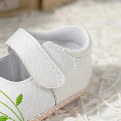 Close-up on the heel and adjustable strap of a white baby girl shoe, highlighting the soft interior padding and stitching detail.