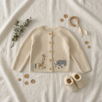Aesthetic baby shower gift flat lay featuring the cream animal knit cardigan paired with matching knit booties, wooden toys, and a eucalyptus branch.