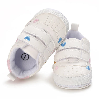 Top-down view of white infant sneakers with heart prints, showing the open double hook-and-loop straps and soft interior lining.