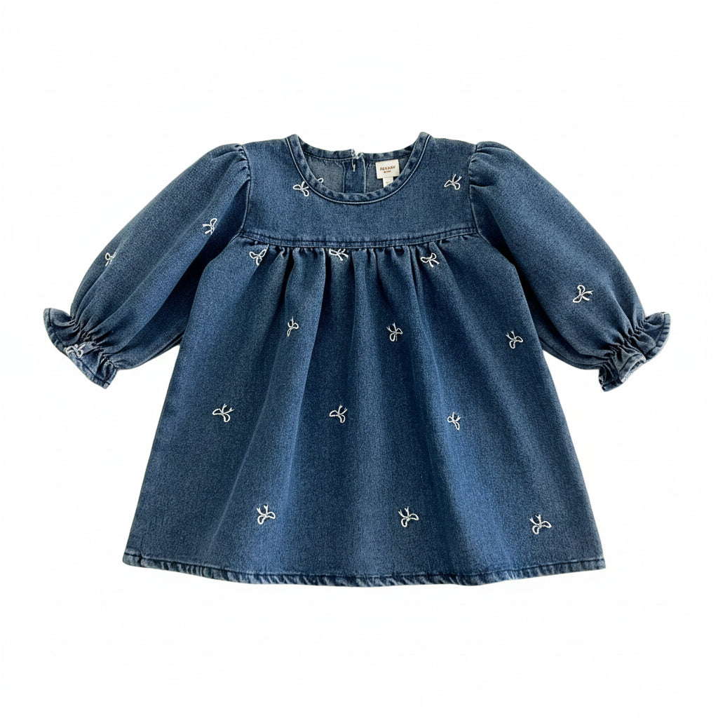Front view of a baby and toddler girl long sleeve blue cotton denim smock dress featuring all-over white embroidered bows.