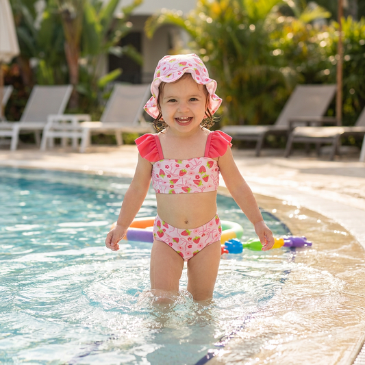 Toddler girl playing at pool wearing a pink strawberry print bikini
