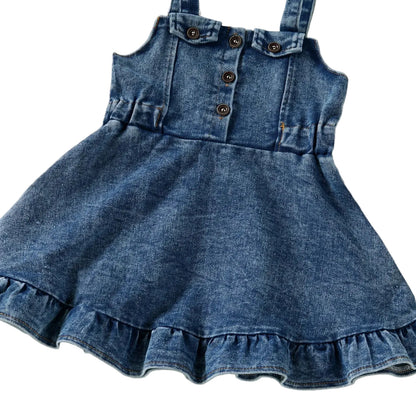 A full front view of the baby and toddler girls blue denim overall dress highlighting the flared A-line silhouette and ruffle bottom.