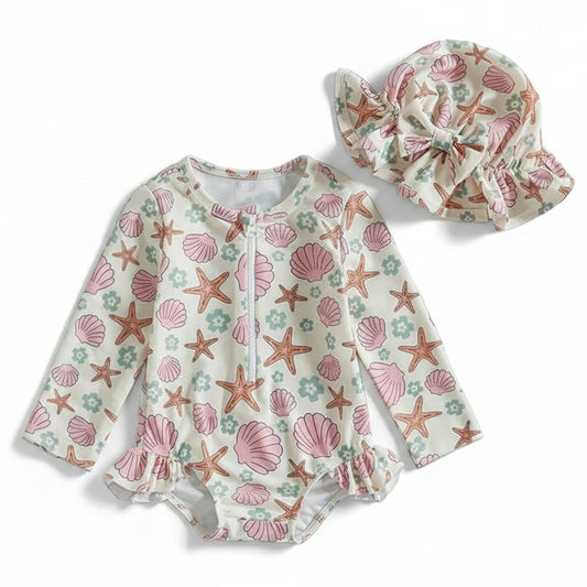 Two-piece infant and toddler girls long sleeve rash guard swimsuit in cream with pink shell and starfish print, featuring a zip-front closure and matching ruffled bow sun hat on a white background.