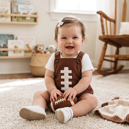 Baby sitting on floor wearing brown corduroy football overall bubble romper game day outfit