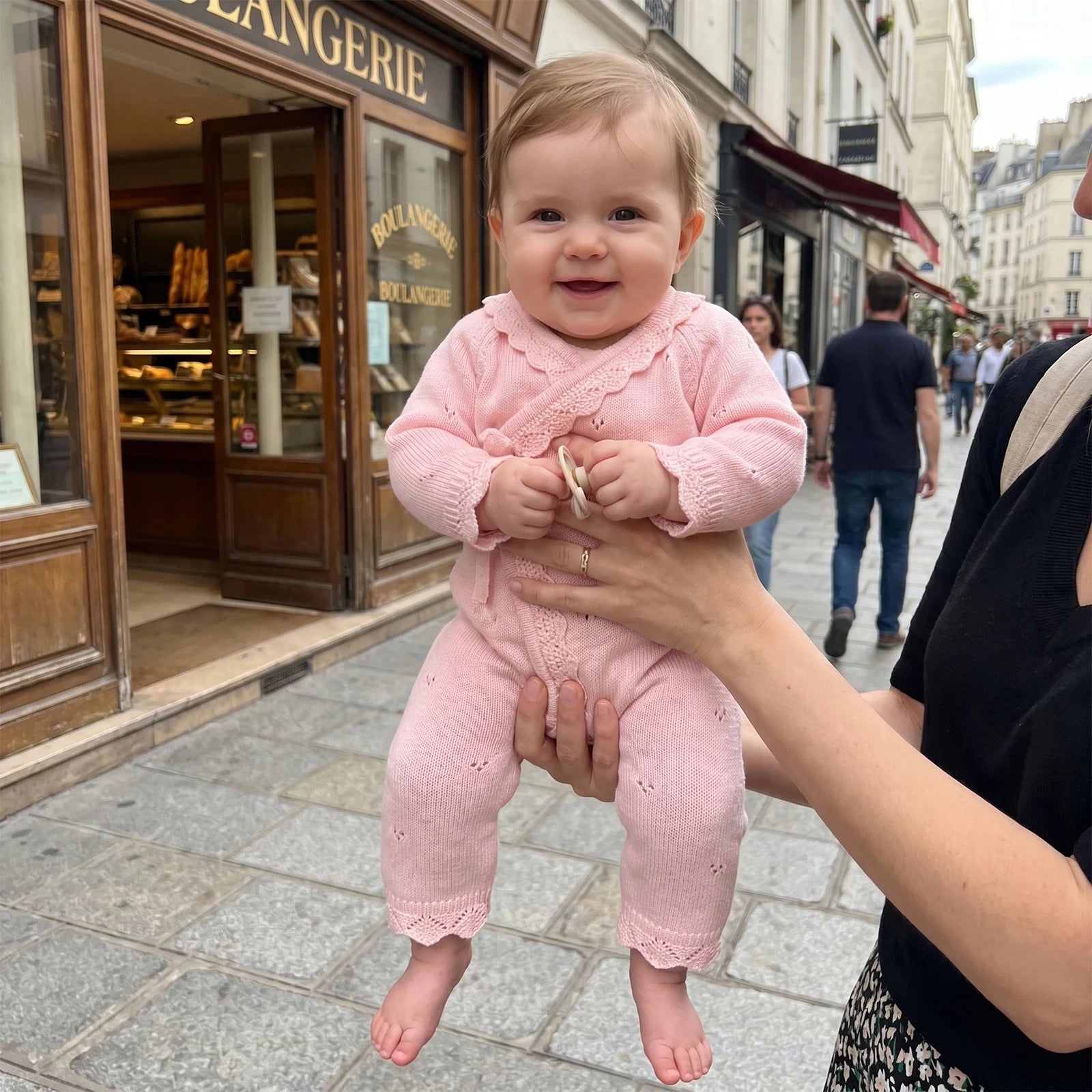 Baby girl being held outdoors on a city sidewalk wearing the pink knit kimono romper.