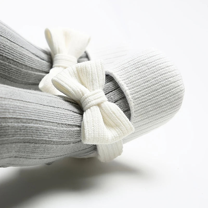 Baby wearing white ribbed knit soft sole Mary Jane crib shoes with grey ribbed tights.