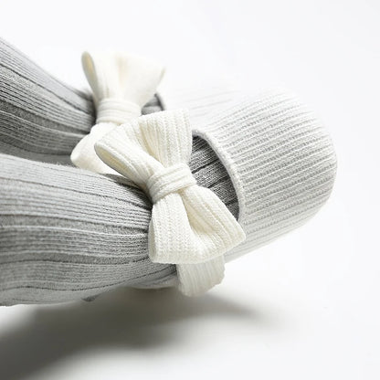 Baby wearing white ribbed knit soft sole Mary Jane crib shoes with grey ribbed tights.