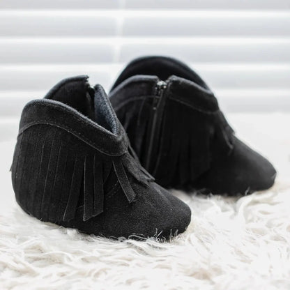 Pair of black baby western fringe moccasin booties, front view on a soft white textured rug.